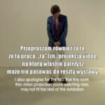 Mężczyzna stoi w jasnej, pustej przestrzeni. Ma opuszczoną głowę w geście skruchy. Białe napisy.